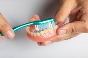 Bạn cần phải vệ sinh răng giả tháo lắp với bàn chải và dung dịch thuốc ngâm